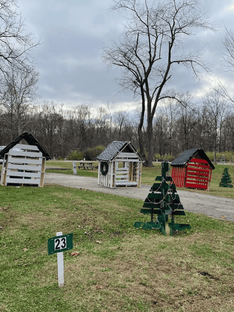 Colorful holiday-themed small wooden houses in a park with leafless trees and cloudy sky, perfect for festive outdoor activities.