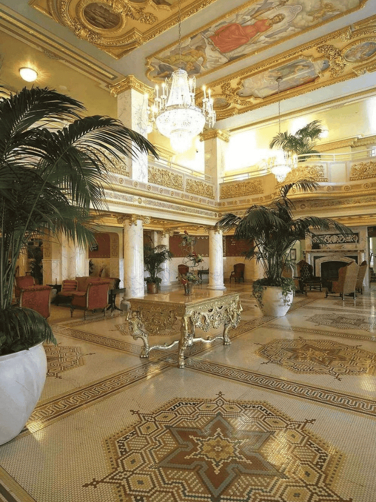 Elegant hotel lobby with gold accents, chandeliers, and lush plants.