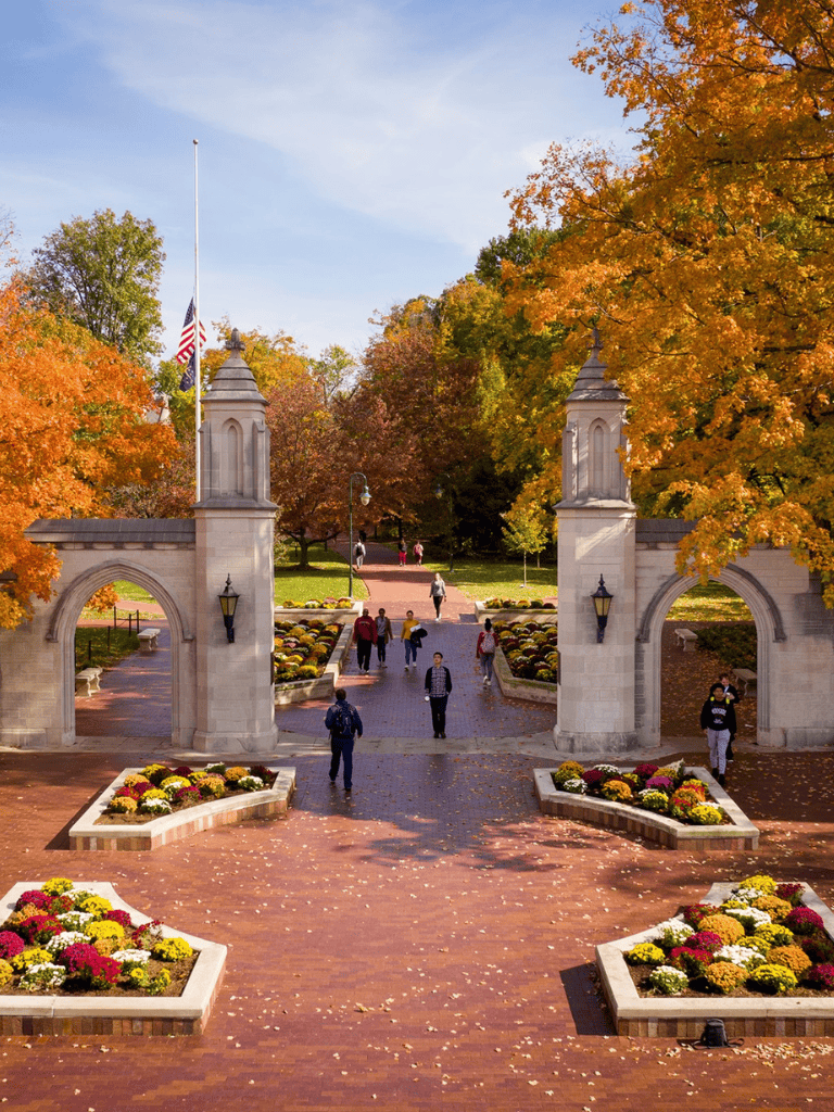 Vibrant autumn foliage at peaceful park entrance with historic archway and visitors walking.