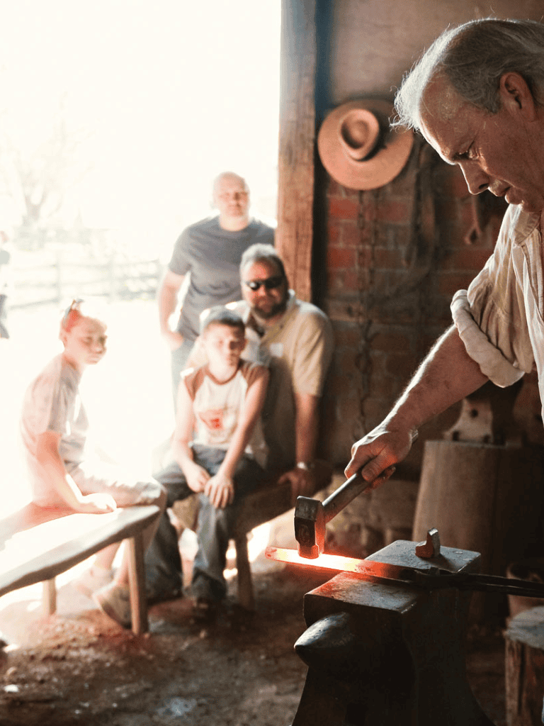 Blacksmith demonstrating metalworking at Quest For Directions event with engaged audience.
