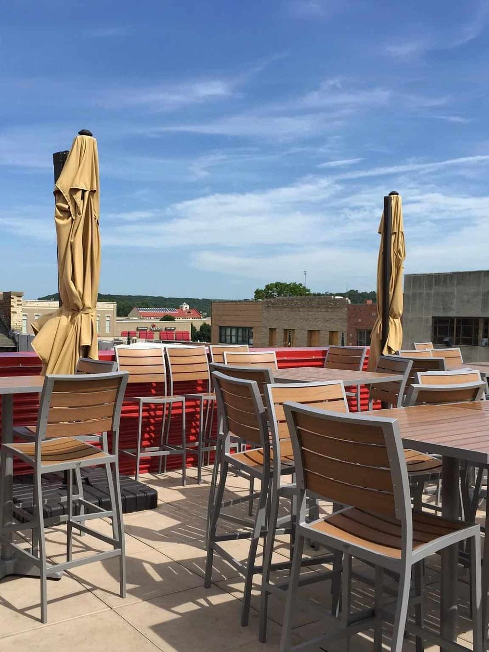 Patio with outdoor seating, umbrellas, and city view on a sunny day.