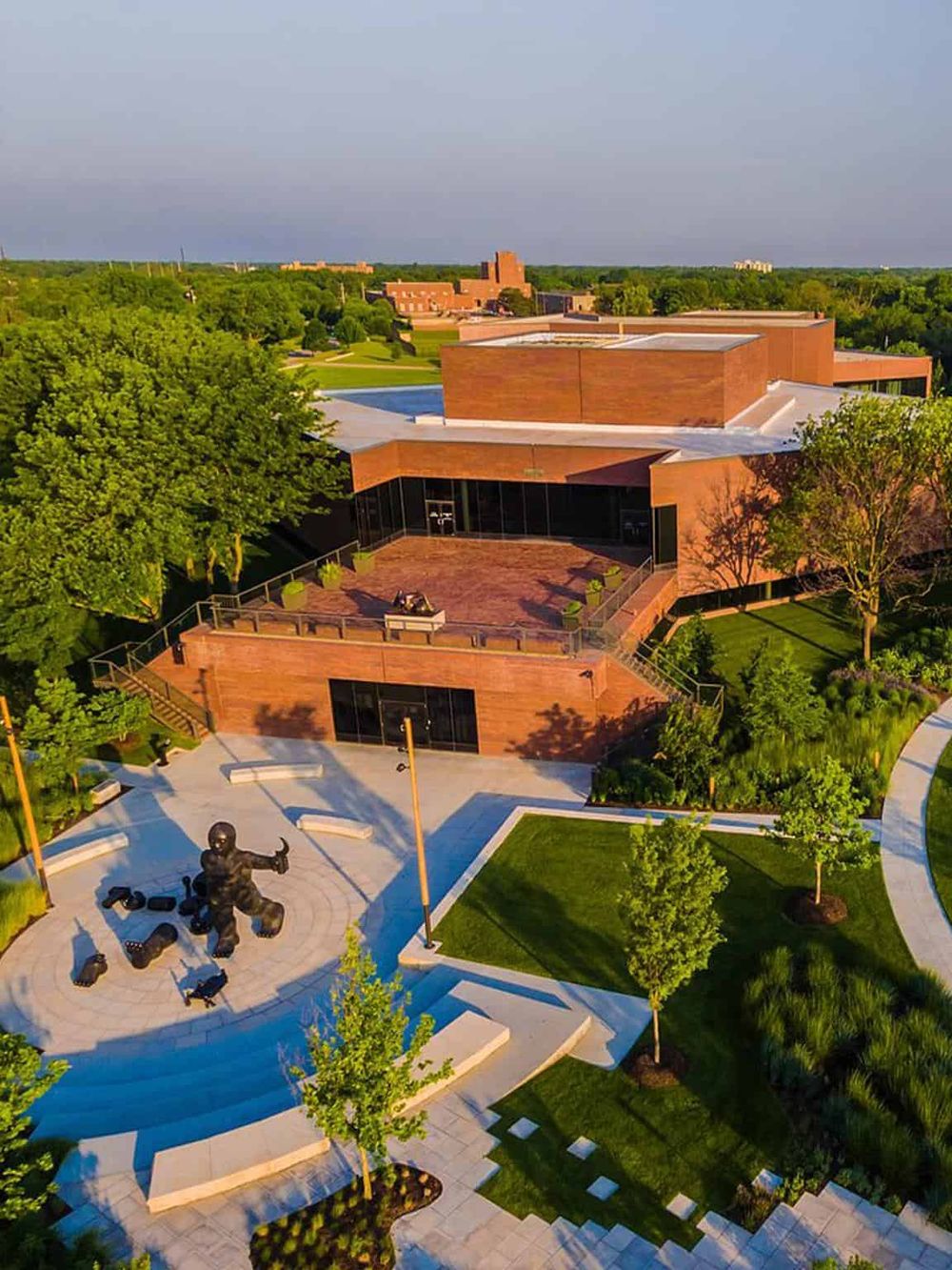 Modern university campus with brick buildings, green outdoor spaces, and a sculpture plaza, located in a scenic, tree-lined environment.