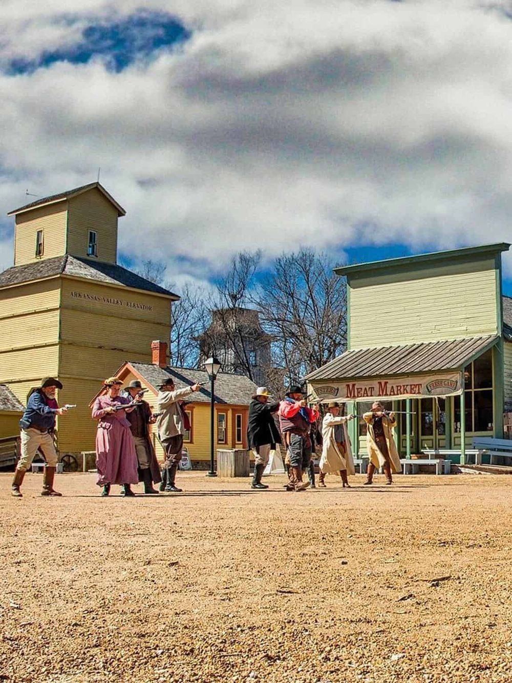 Historical Wild West town reenactment with actors in period costumes and vintage buildings.