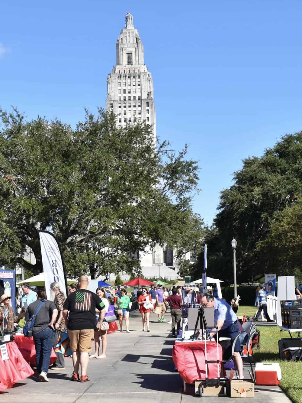 Vibrant outdoor market in front of a historic skyscraper, bustling with people and vendors during daytime.