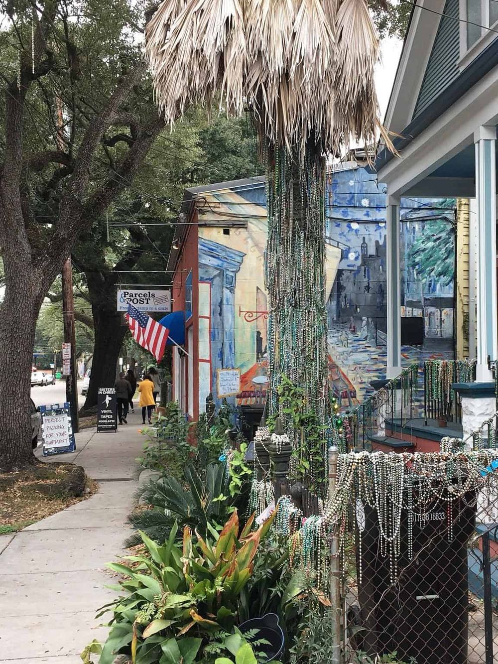 Colorful bead jewelry display outside shop on vibrant city street with mural art backdrop.