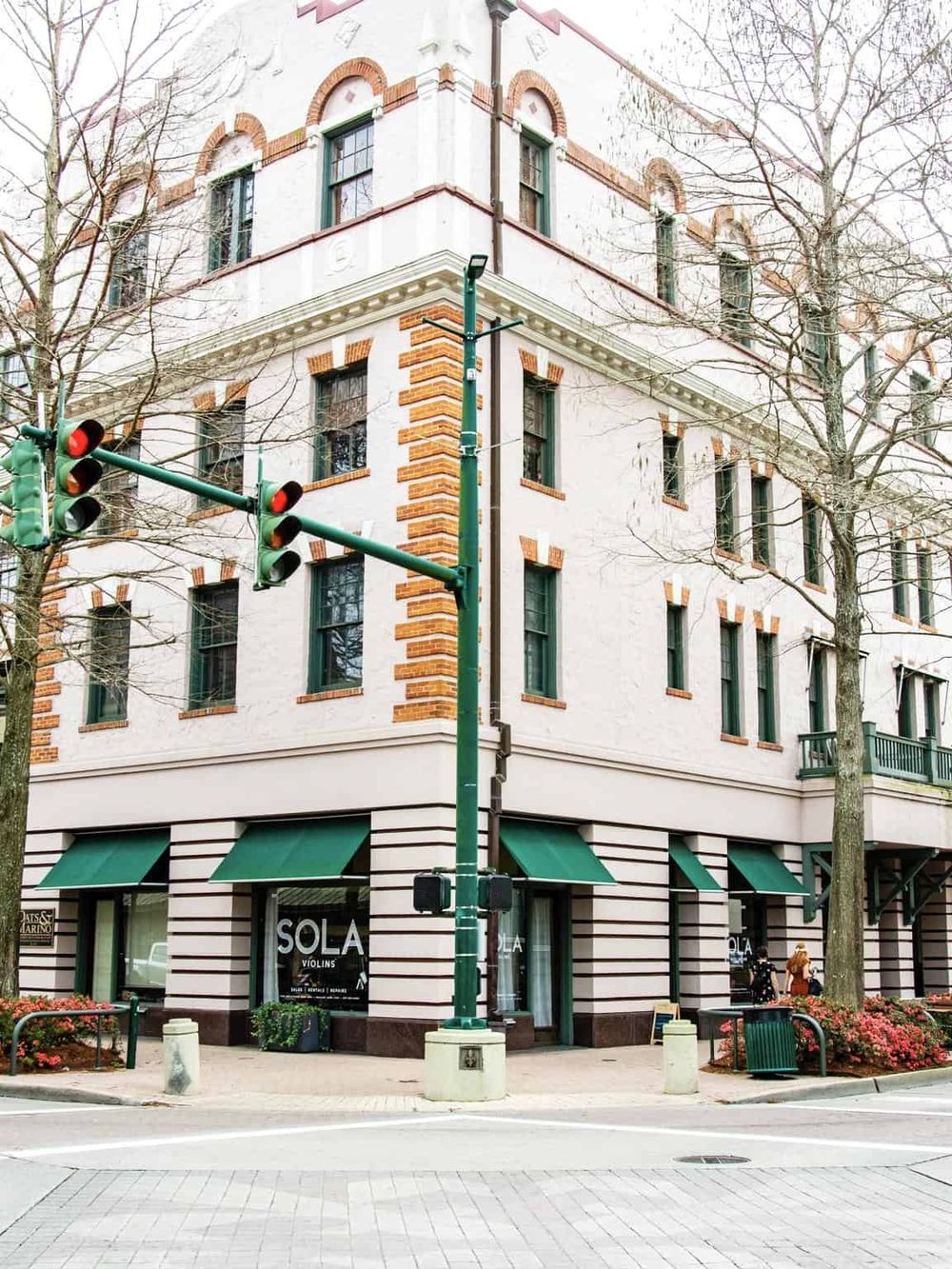 Colorful urban corner building with storefronts, traffic lights, and trees in downtown area.