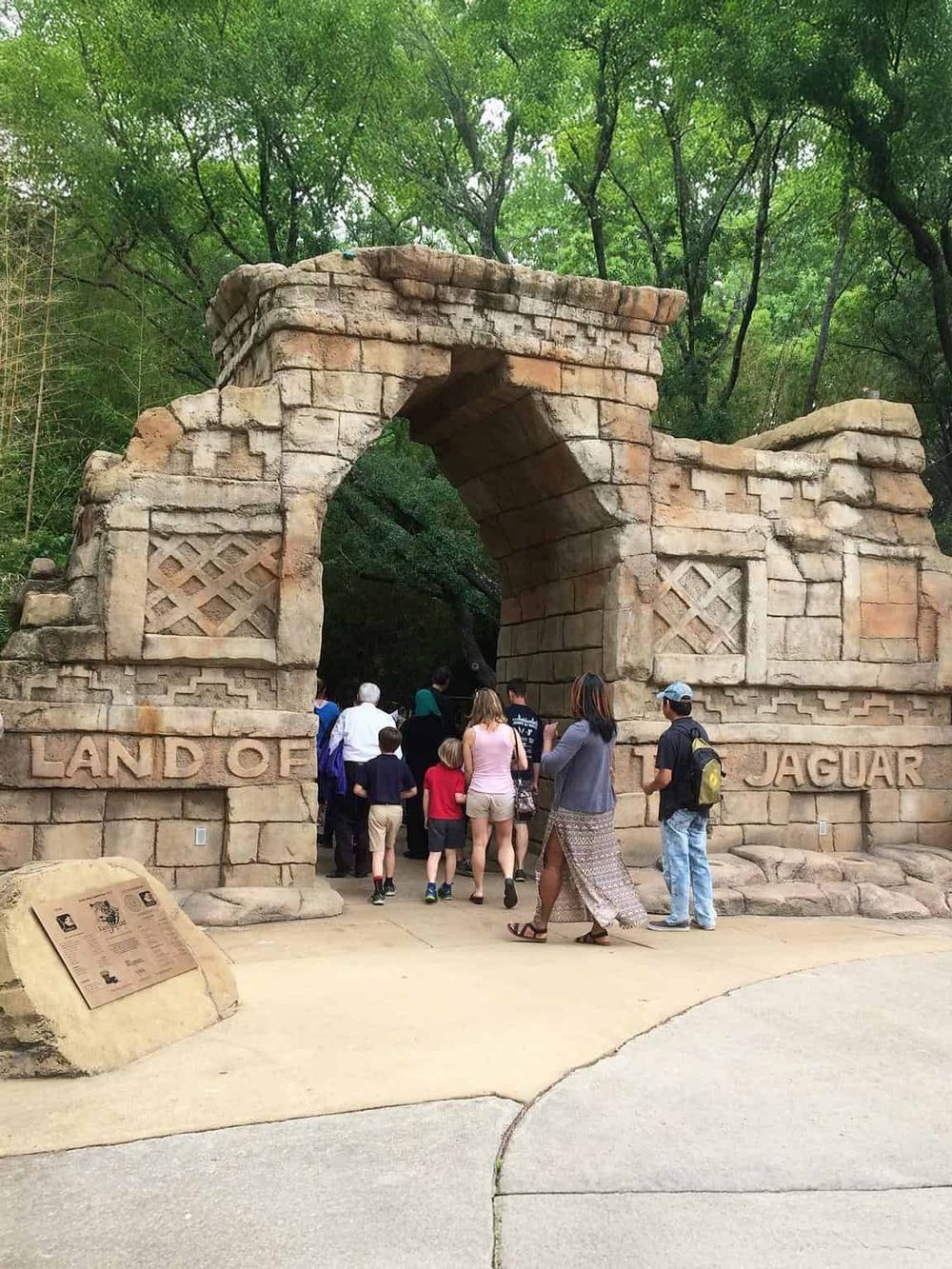 Ancient stone arch entrance at Jaguar Land Rover Experience, surrounded by lush green trees in a natural setting.