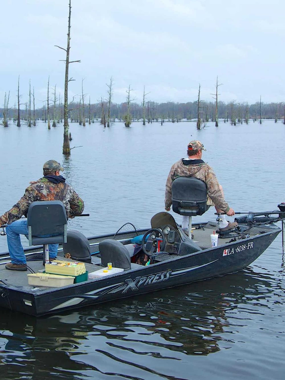 Fishermen on a boat in a swampy wetland area with dead trees, showcasing outdoor adventure and fishing experiences.