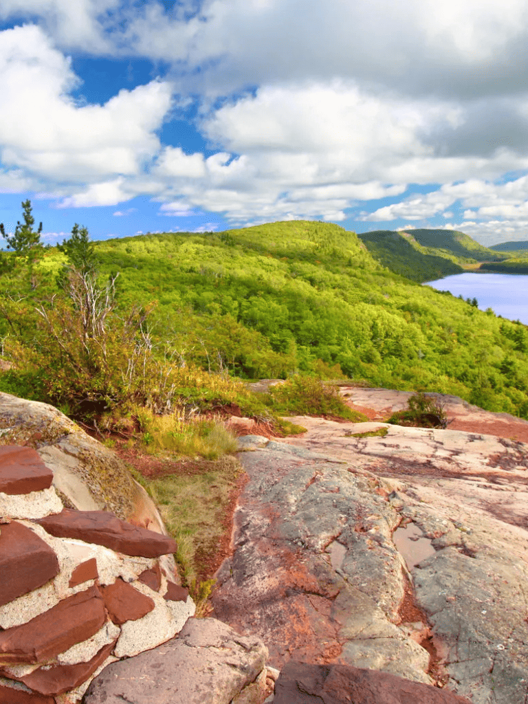 Vast green hillside with rocky foreground and bright blue sky, scenic outdoor landscape for adventure and nature lovers.