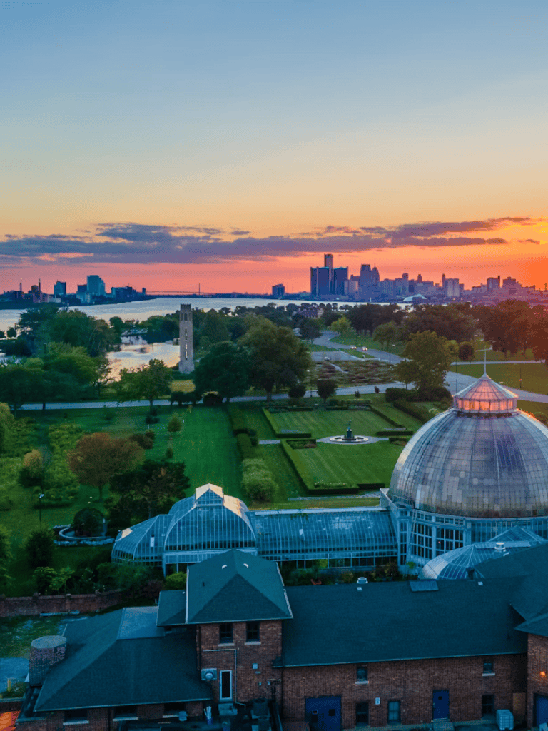 Aerial view of downtown city skyline with Riverwalk, green parks, and botanical gardens at sunset, showcasing quest for directions.