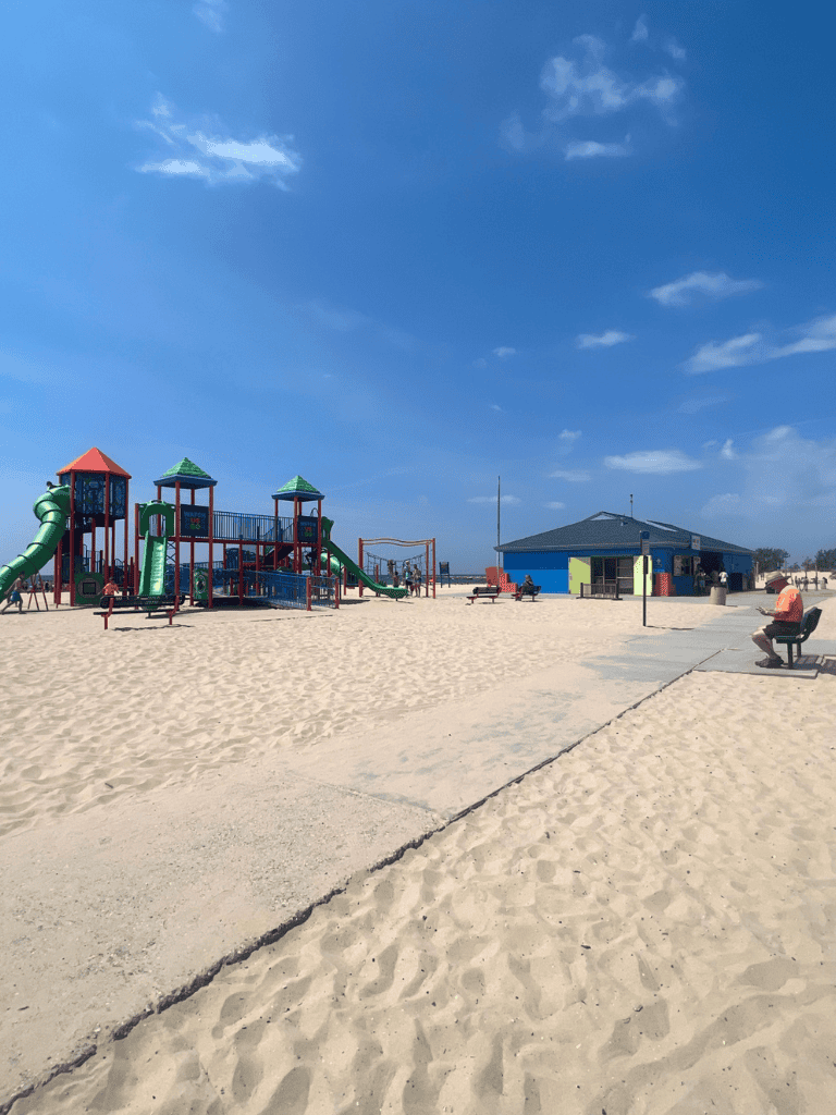 Colorful beach playground structure with slides and swings on sandy beach under blue sky.
