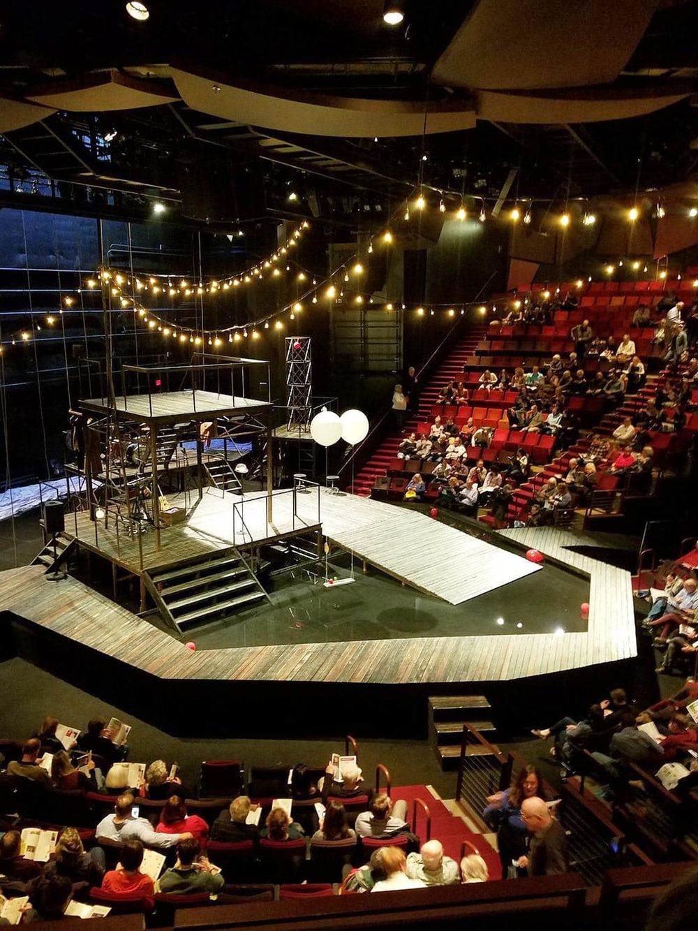 Vibrant theater stage with set design for a live performance, surrounded by an engaged audience in a modern auditorium.