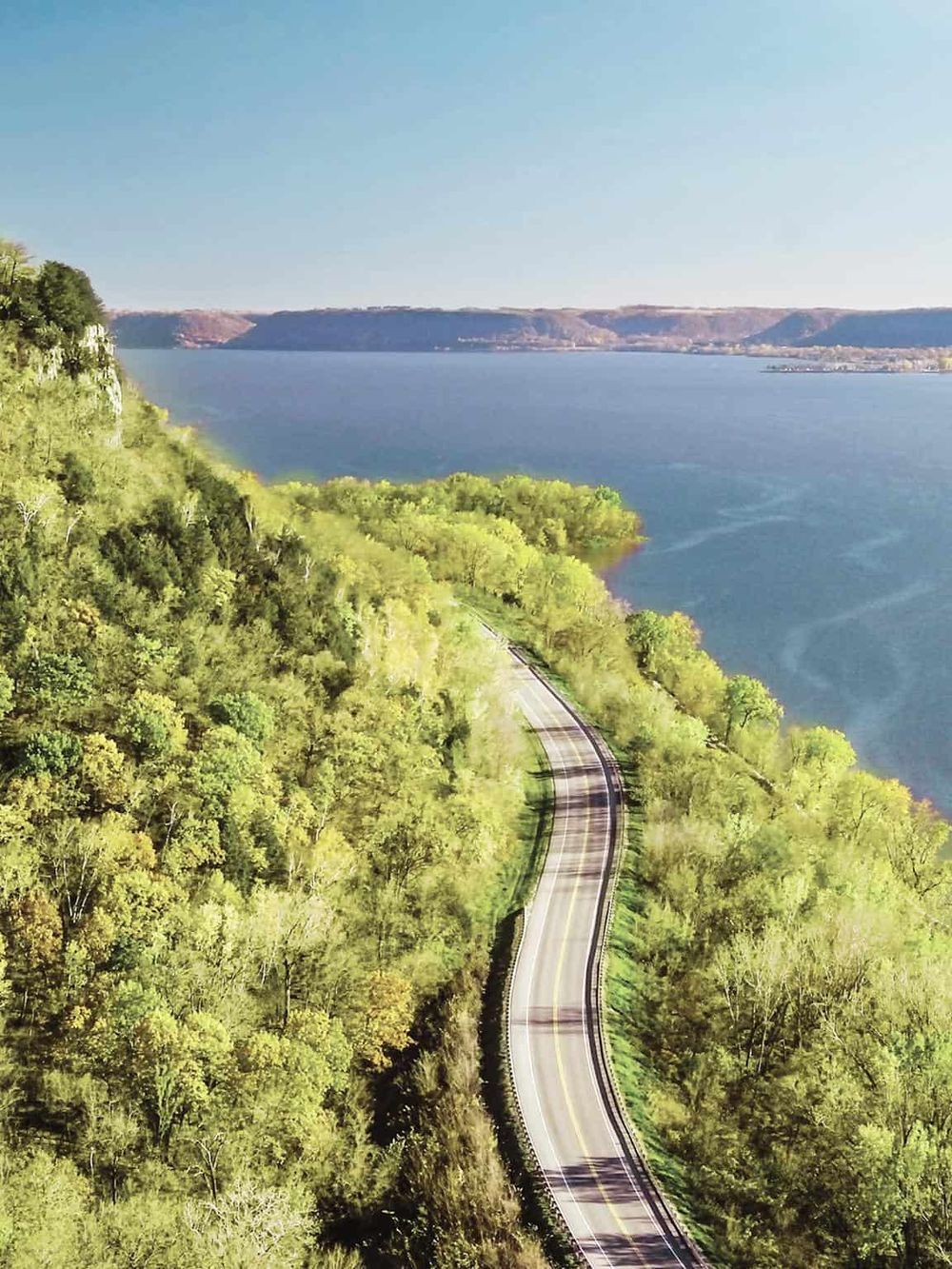 Rolling scenic road along Lake, lush green trees and clear blue sky, adventure, travel, explore nature.