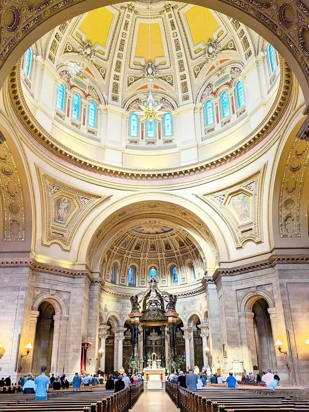 Elegant church interior with detailed architecture, stained glass windows, and worshippers in prayer.