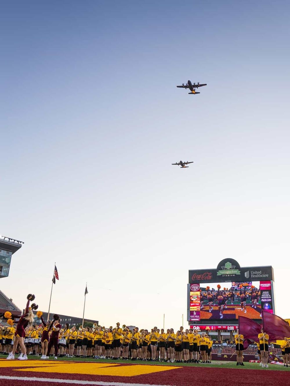 Airplanes flying over stadium with cheerleaders and audience.