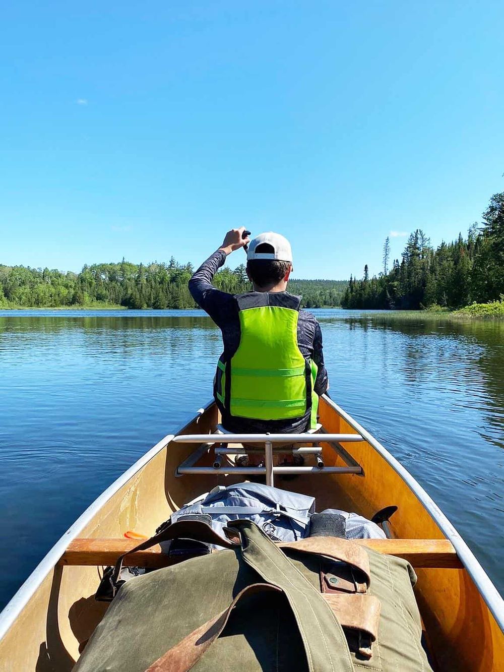 Serene canoeing on a calm river surrounded by lush green trees under a clear blue sky.