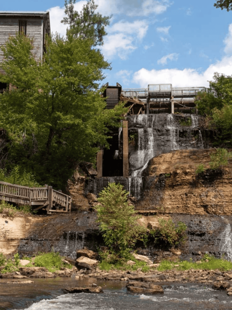 Waterfall with scenic outdoor setting and wooden bridge in a lush forested area, ideal for nature tourism.