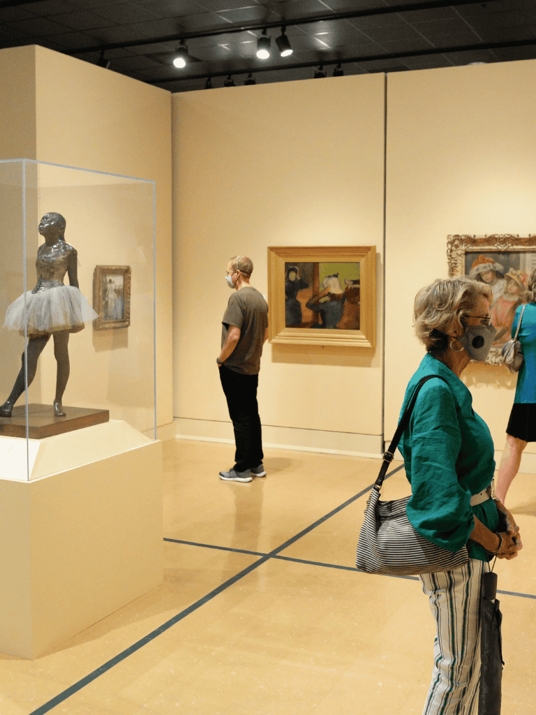 Girl in green jacket viewing art at QuestForDirections gallery, museum visitors appreciating fine art exhibits.
