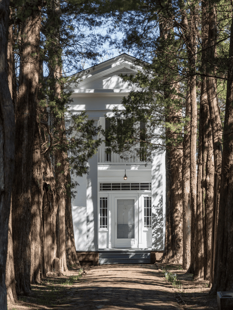 Timeless white house surrounded by tall trees, scenic nature, and inviting front porch for serene living.