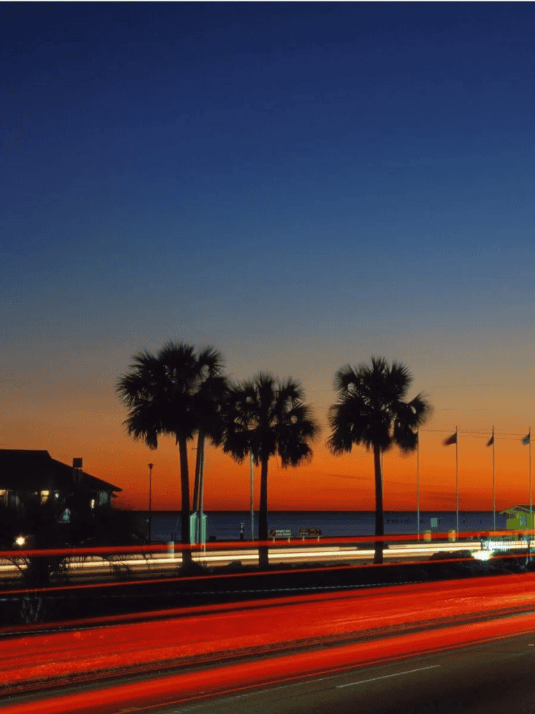 Aerial view of sunset over beach with palm trees and vibrant sky in Florida, ideal for travel and vacation planning.