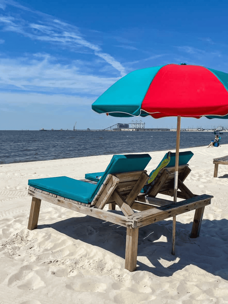 Beach chair and umbrella on sandy shore with ocean view and distant pier | QuestForDirections.
