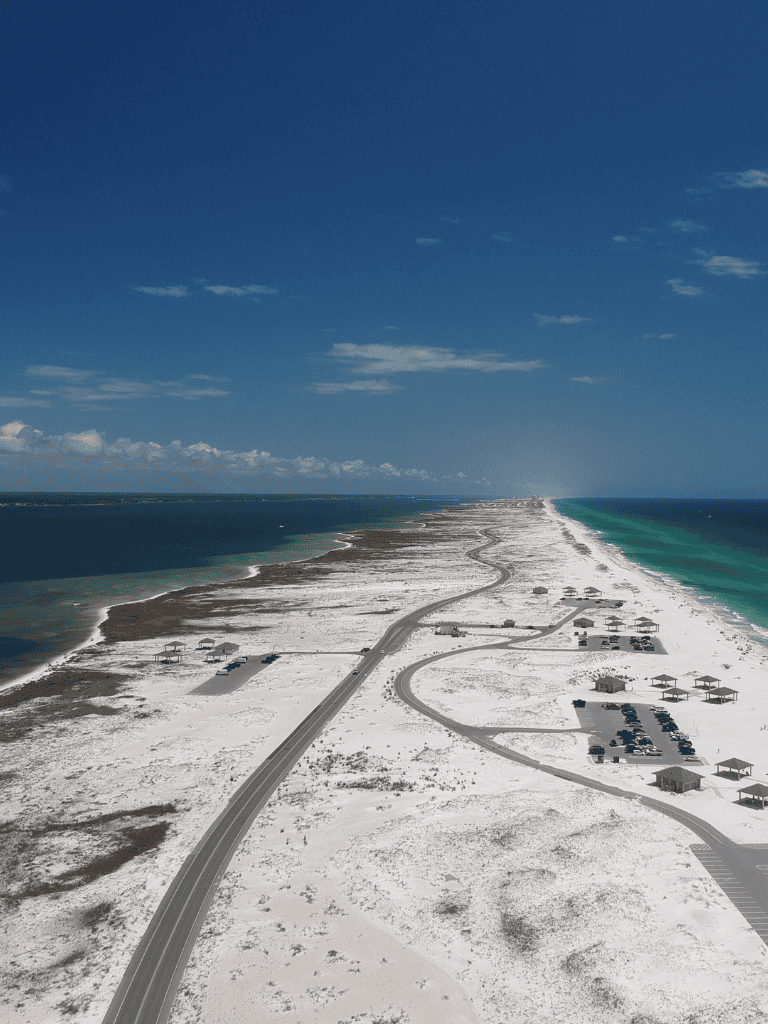 Seaside coastal road with beach houses and clear ocean water under a bright blue sky.