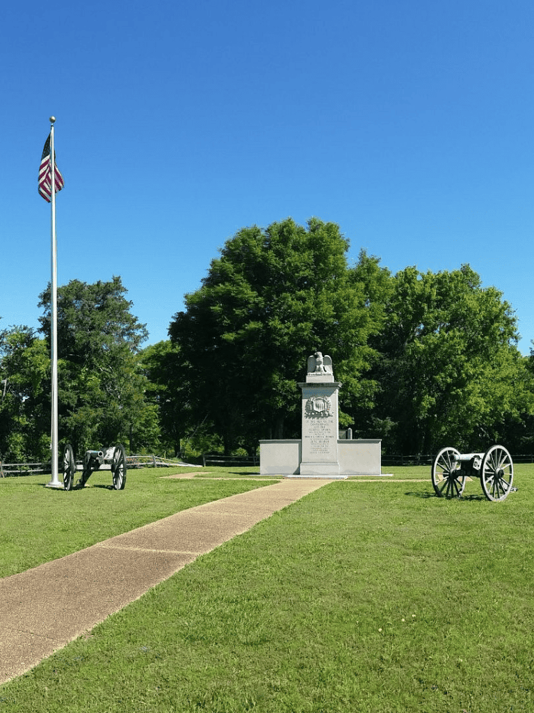 American flag flying near Civil War cannon and monument in park.