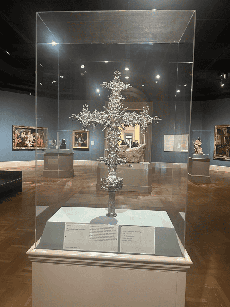Intricate silver cross sculpture displayed in a museum exhibit, showcasing historical religious artifacts and fine craftsmanship.