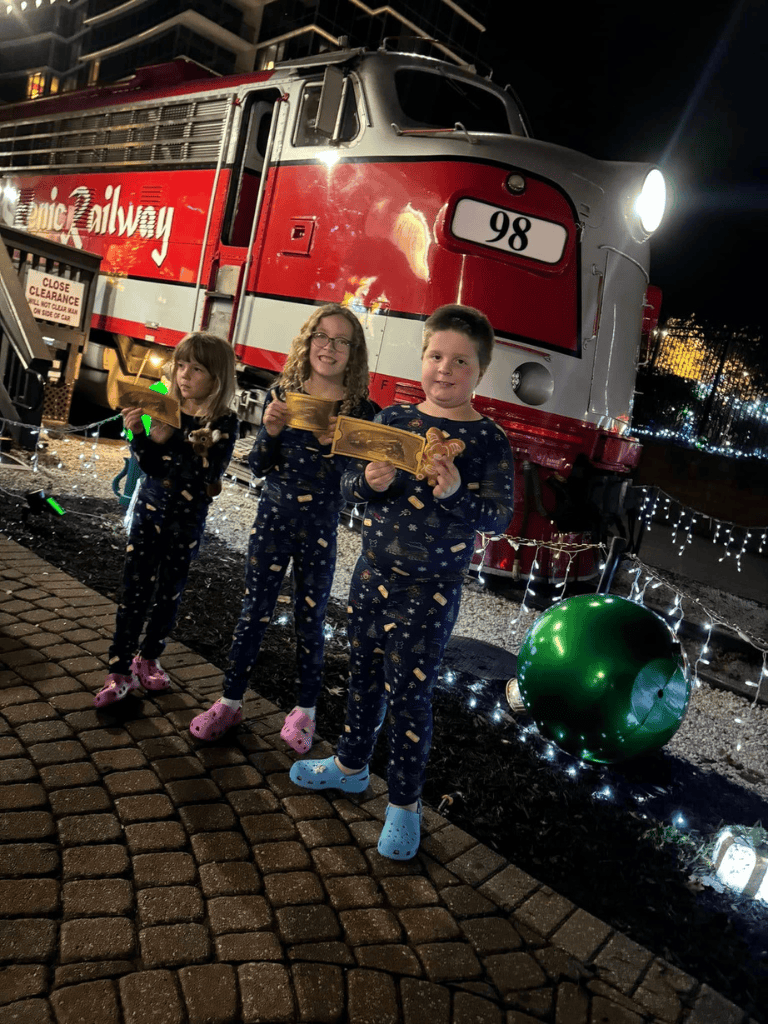 Festive holiday train display with children enjoying Christmas decorations and lights.