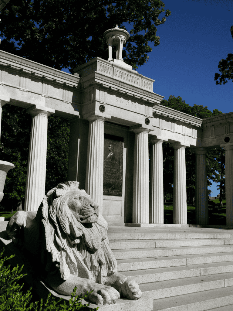 Majestic marble lion and historic memorial with columns at Swope Park, guiding visitors to local landmarks.