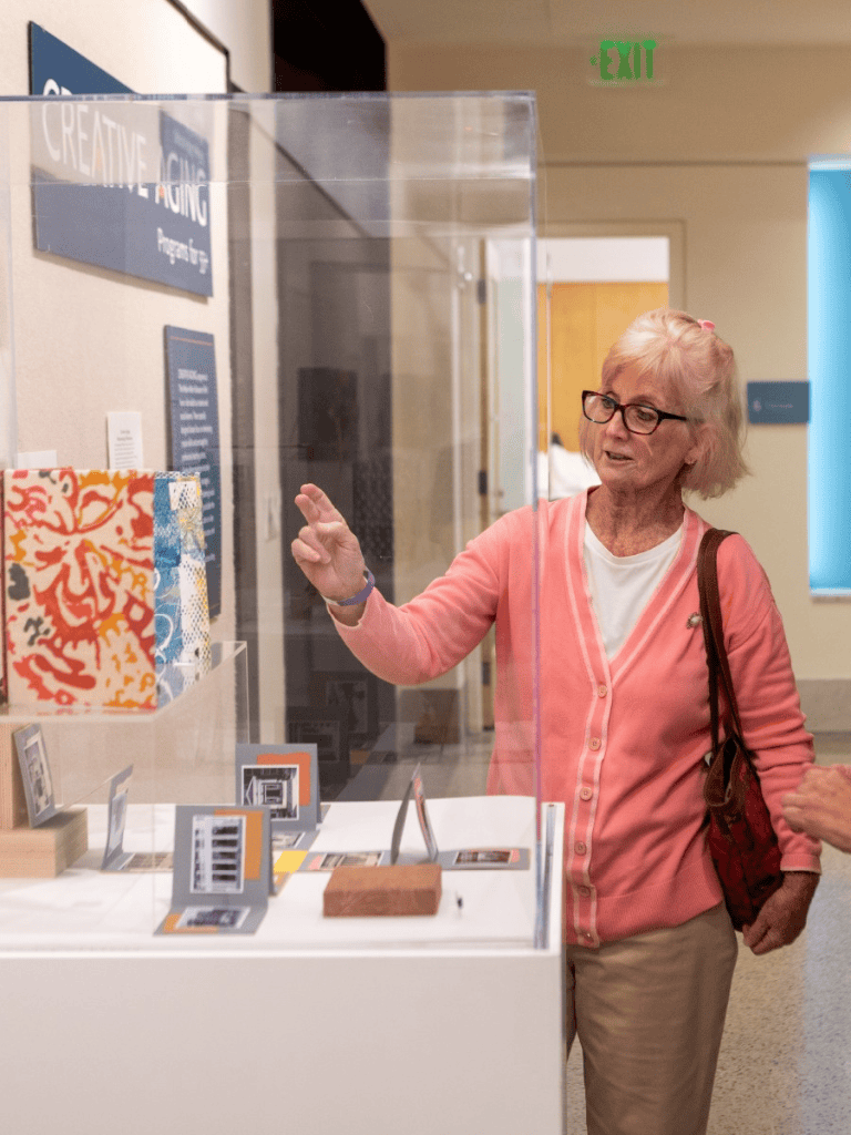 A woman viewing artwork behind a glass display case at an art gallery or exhibit.