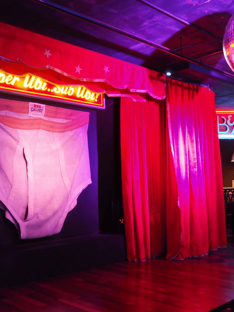 Hotdog and sub food stage at QuestForDirections entertainment venue in vibrant pink and red lighting.