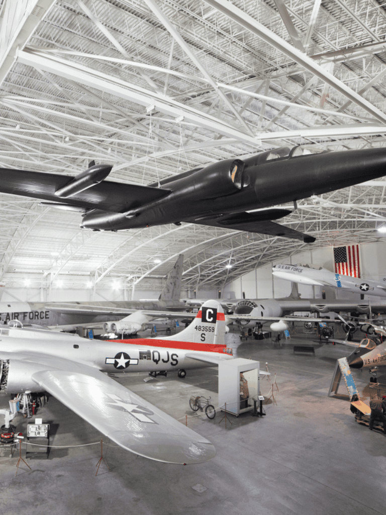 Black stealth aircraft displayed in a museum with vintage planes.