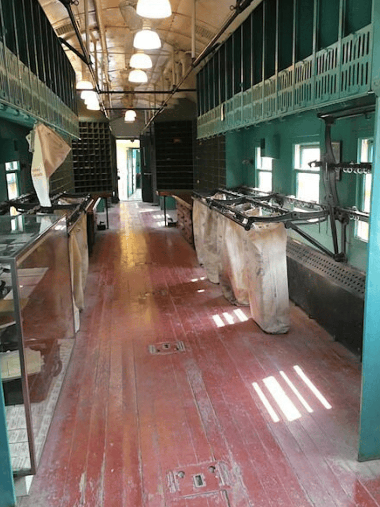 Empty vintage train car with luggage racks, worn wooden floor, and natural light from windows, part of QuestForDirections.