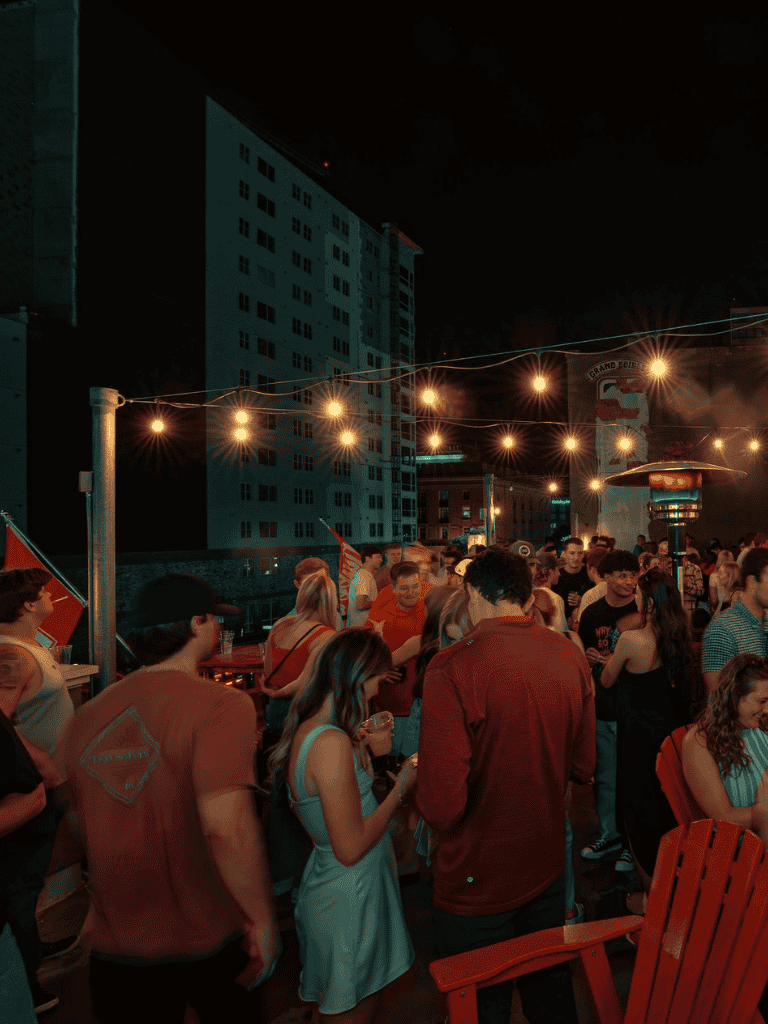 Night outdoor gathering with string lights, diverse group, city buildings, casual social event.