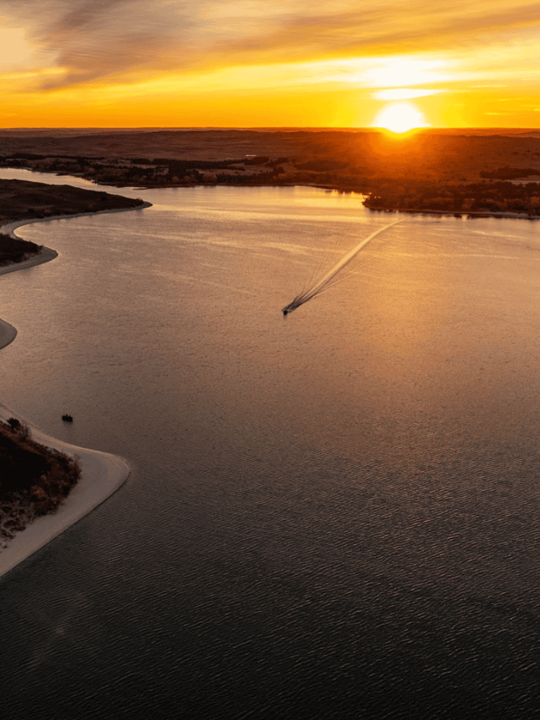 Serene river landscape at sunset with a boat creating waves, ideal for outdoor adventure and navigation.