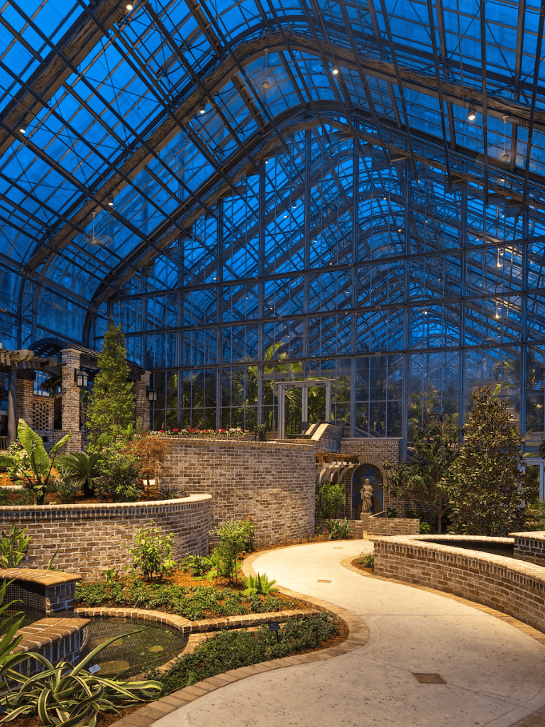 Lush indoor botanical garden with glass greenhouse, tropical plants, and winding path.