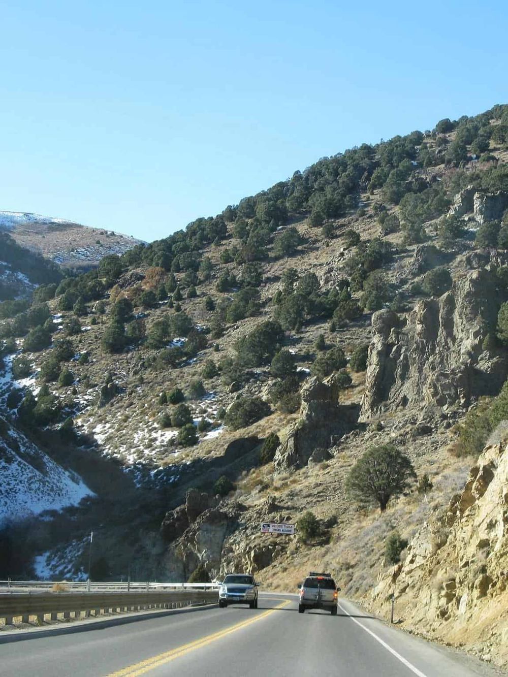 Highway driving through mountainous terrain with trees and rocky cliffs, scenic outdoor adventure and travel.