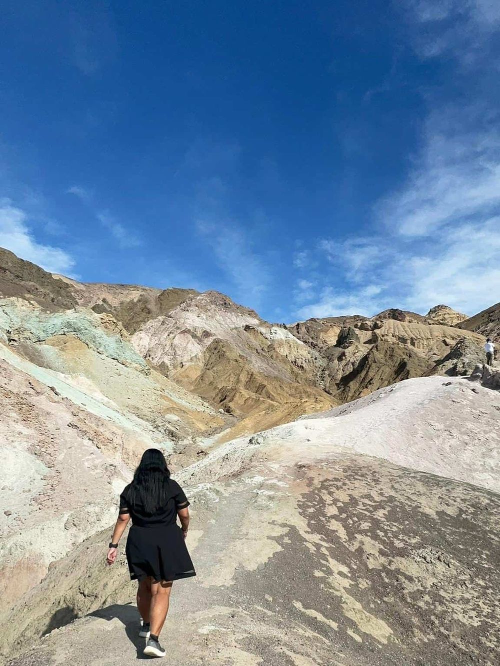 Breathtaking desert landscape with colorful mountains and a woman hiking under a clear blue sky.