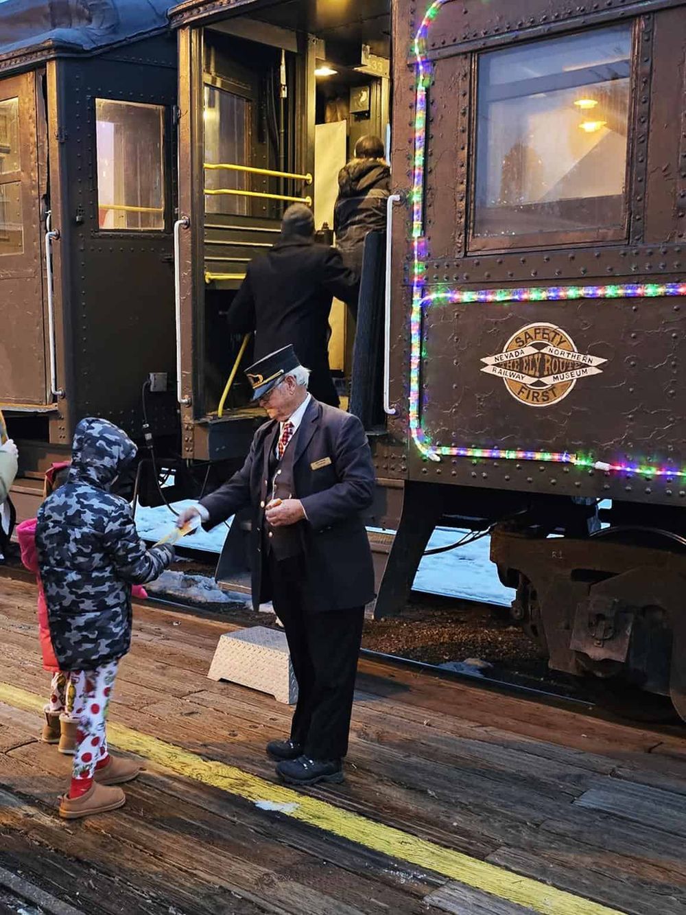 Vintage train conductor assisting a passenger at a historic railway station, festive holiday atmosphere, detailed railway car.