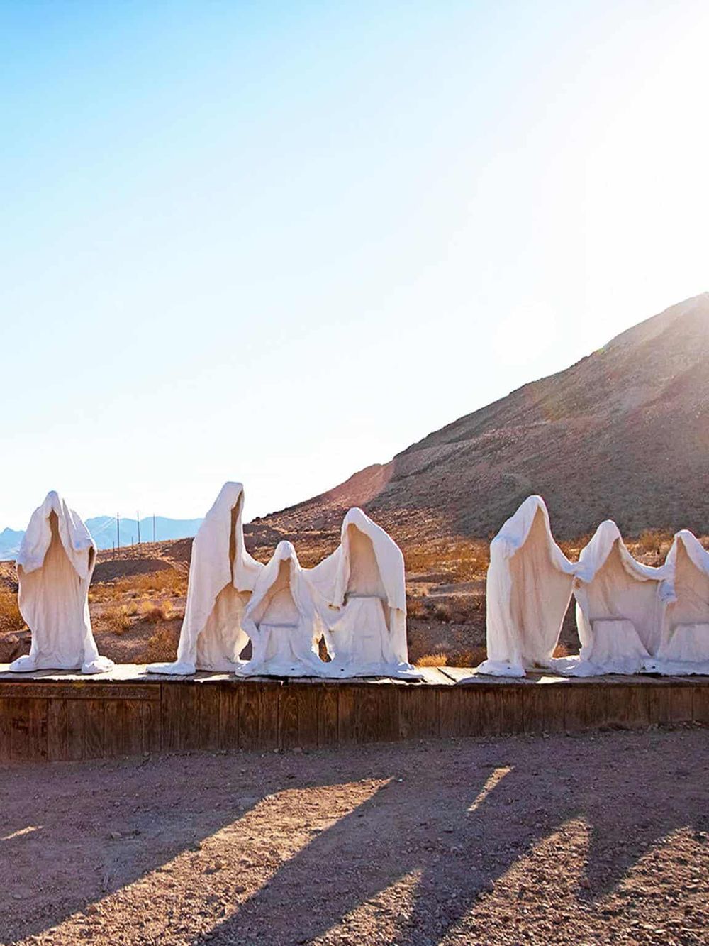 Colorful metal sculptures of people with white cloaks in a desert landscape at sunset.