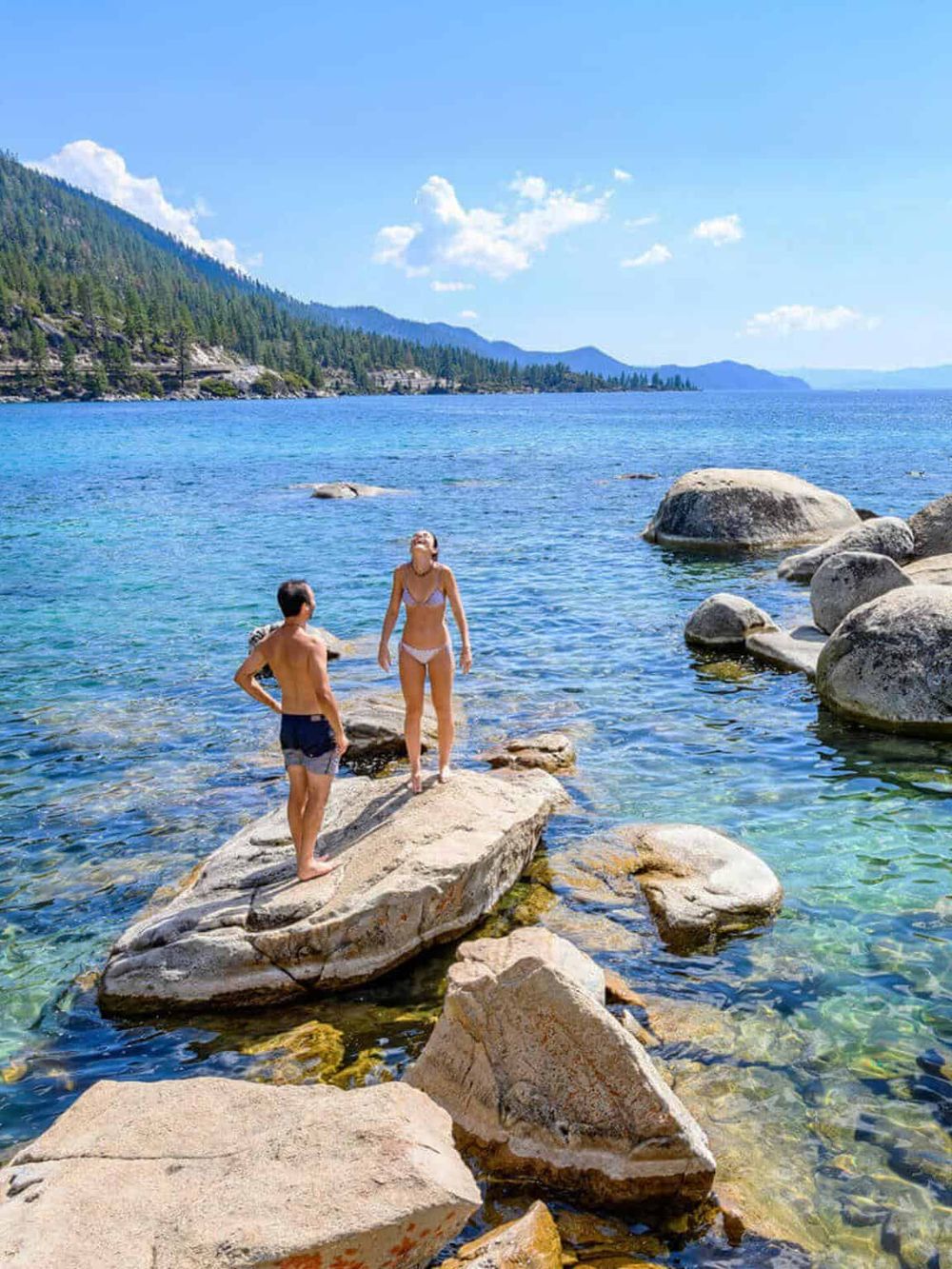 Serene lakeside scene with two people enjoying the clear water and scenic mountain views.