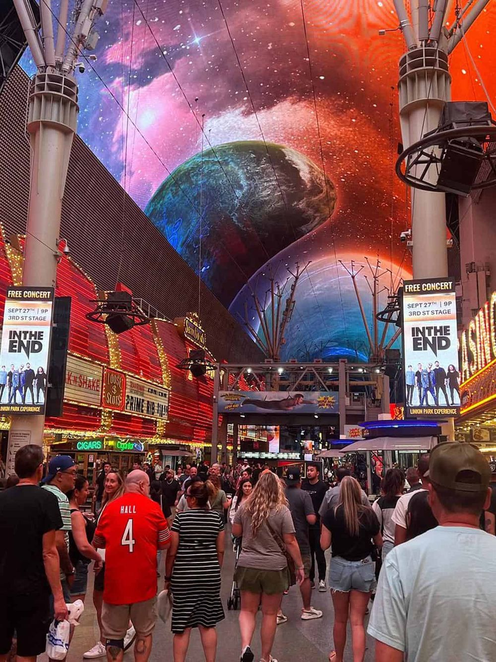 Colorful Las Vegas Strip scene with digital space-themed art overhead, lively crowd, and neon signage.