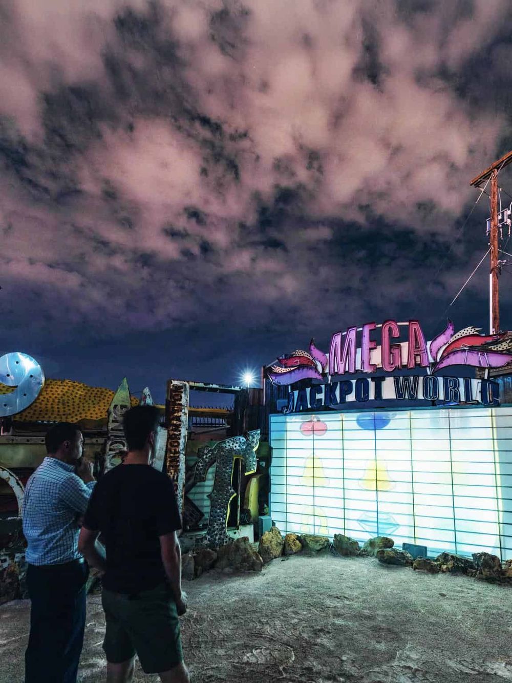 Bright neon sign at a carnival or fairground with cloudy night sky, showcasing entertainment venues and amusement rides.
