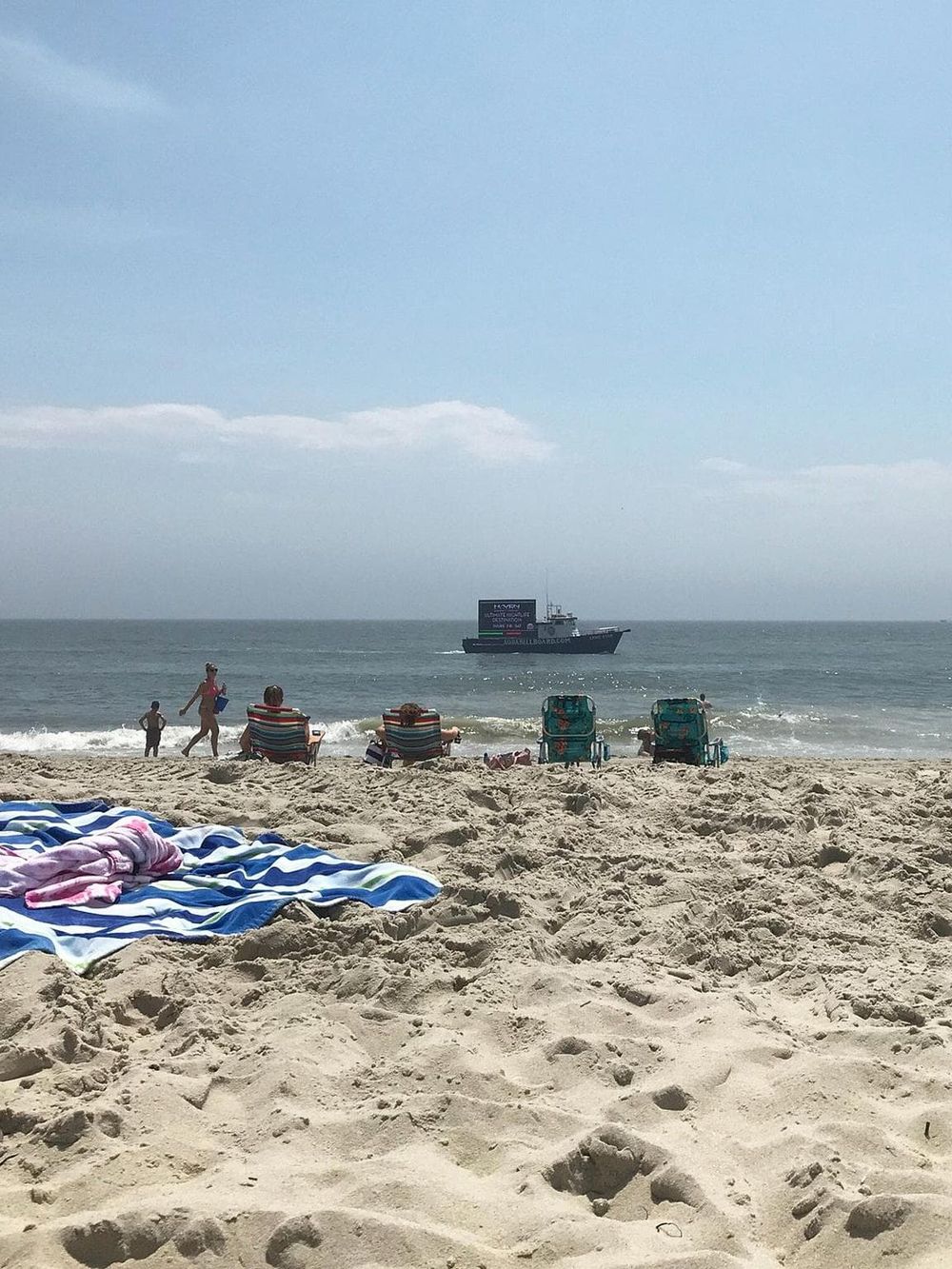 Beach with sand, ocean, and boating scene, people relaxing and enjoying seaside view.