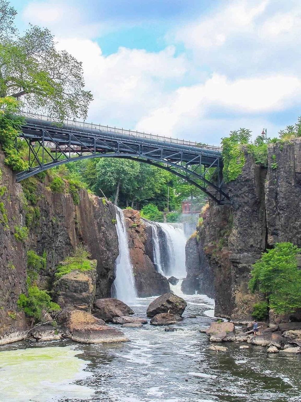 Waterfall with bridge and lush greenery, scenic outdoor adventure destination.