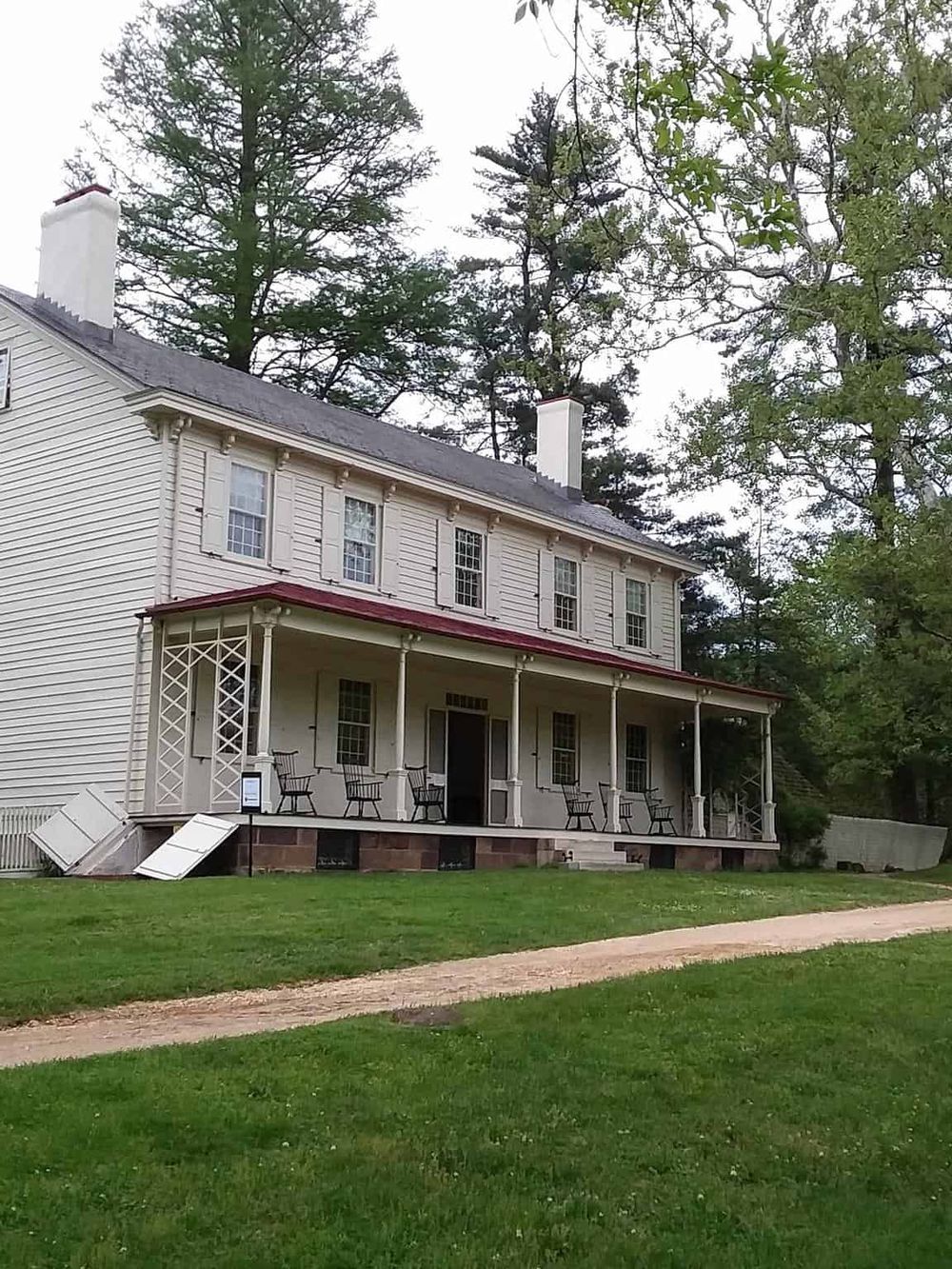 Charming historic house with a large front porch and lush green surroundings, perfect for exploration and directions.