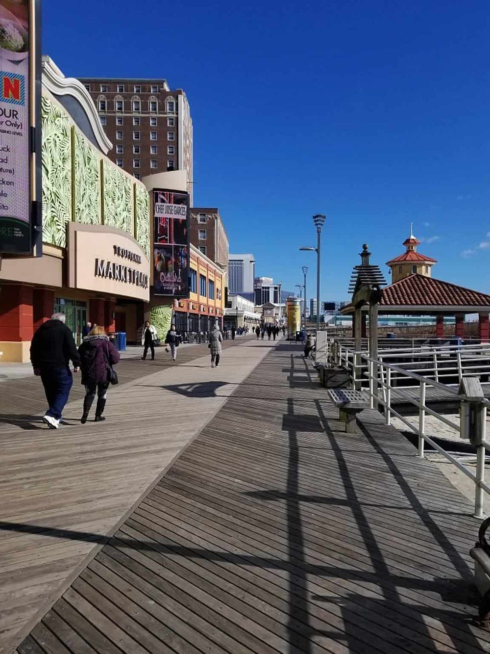 Bright wooden boardwalk along Atlantic City seaside with shopping and entertainment venues.