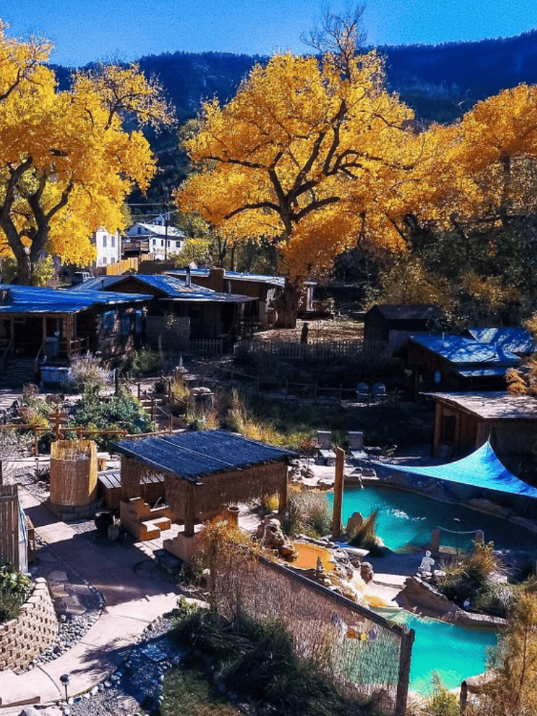 Colorful fall scene with trees, cabins, and a hot tub in a scenic mountain setting.