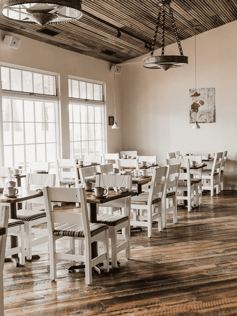 Cozy dining area with wooden flooring, white chairs, large windows, and rustic decor - QuestForDirections.